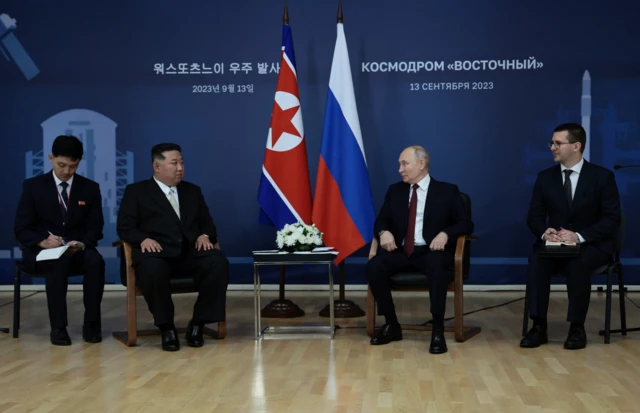 Kim and Putin sitting in front of Russian and North Korean flags with attendants on either side