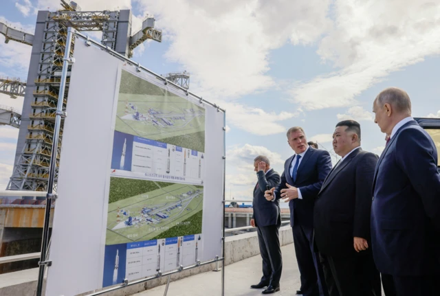 An official speaking to Putin and Kim Jong Un in front of a chart about Russia's space programme