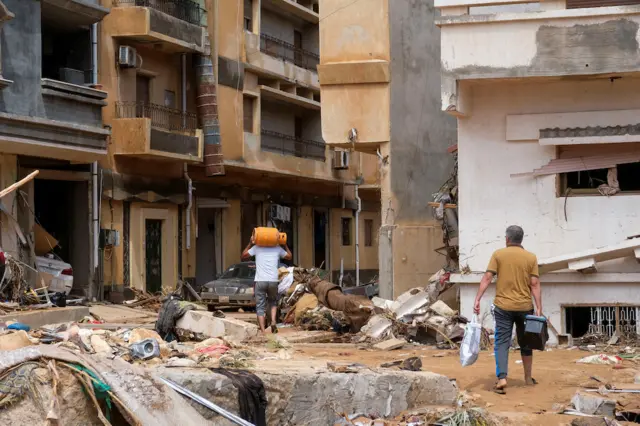 People walk between the debris, after a powerful storm and heavy rainfall hit Libya, in Derna