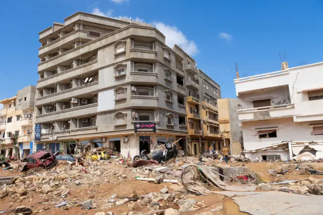 Rubble, upturned cars and other debris litters the street outside a building in Derna