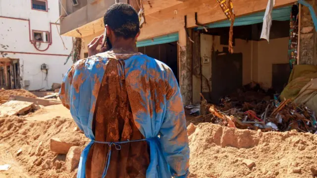 A man in muddy scrubs speaks on a phone