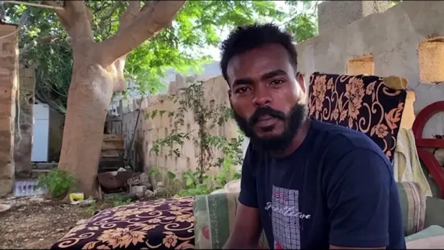 Wali Eddin Mohamed sits on a blanket on the ground under a tree