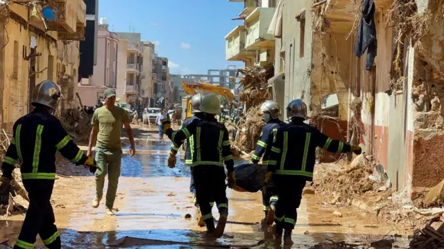 Members of the rescue teams from the Egyptian army carry a dead body as they walk in the mud between the destroyed buildings, after a powerful storm and heavy rainfall hit Libya, in Derna, Libya September 13, 2023.