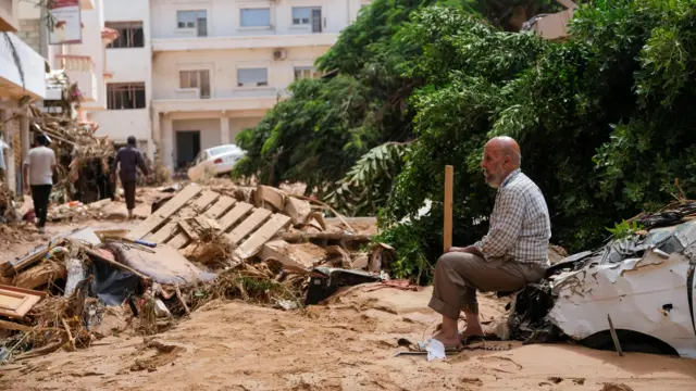 A man sits on a damaged car, after a powerful storm and heavy rainfall hit Libya, in Derna