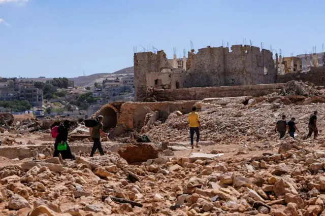 People walk amidst the debris, following a powerful storm and heavy rainfall hitting the country, in Derna