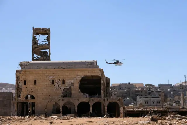 A helicopter flies over damaged buildings, after a powerful storm and heavy rainfall hit Libya