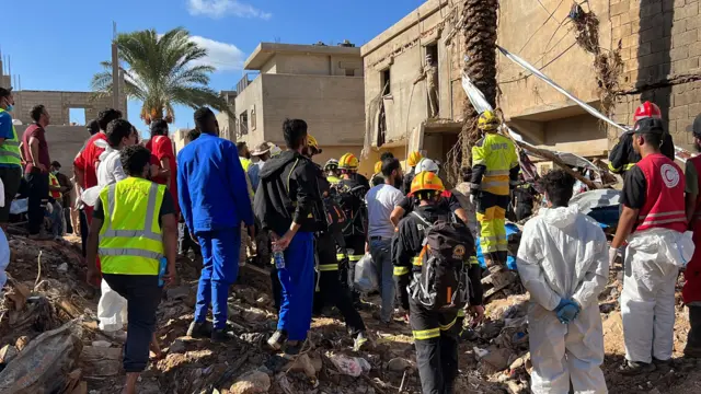 A group of rescue workers, including Red Crescent personnel, stand on the rubble in Derna