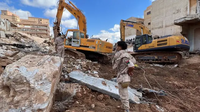 A rescue worker looks on as two excavators try to move some rubble in Derna