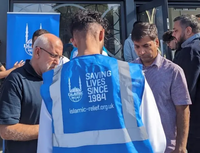 Islamic Relief charity worker collecting donations from two men outside a mosque