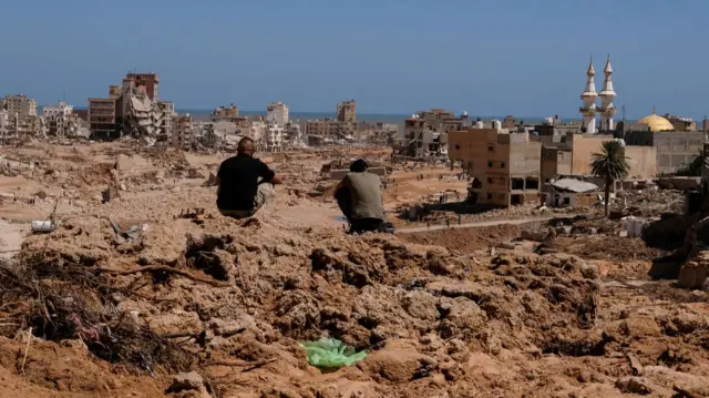 Two men sit atop a mountain of mud in Derna on 14 September