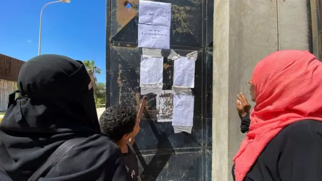 People look at the list of missing people taped to a door, in Derna, September 14, 2023