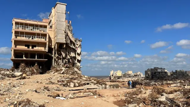 People walk through the area of Derna where the entire neighbourhood was washed away. One half of an apartment building still stands