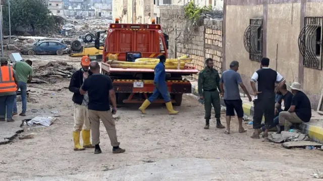 Aid workers and survivors speak, standing on a street littered with debris in Derna on 14 September 2023