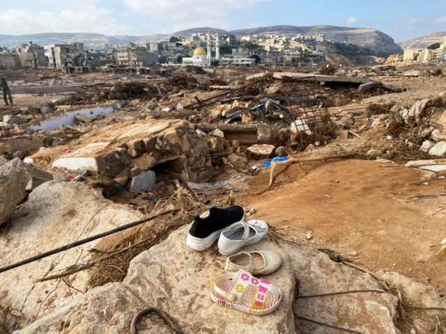 Children shoes are placed on a rock with a view of the devastation in Derna in the background