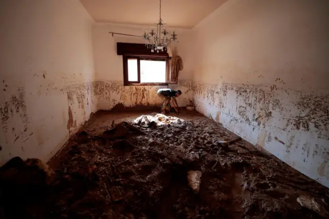 A survivor clears mud out of his house