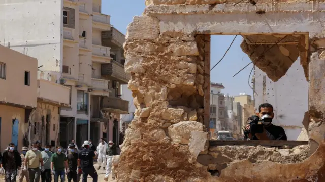 A journalist stands inside a destroyed building while search teams and volunteers walk, following fatal floods in Derna, Libya - 19 September 2023