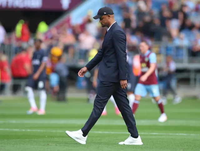 Vincent Kompany walks across the pitch in suit and cap with his eyes on the floor.