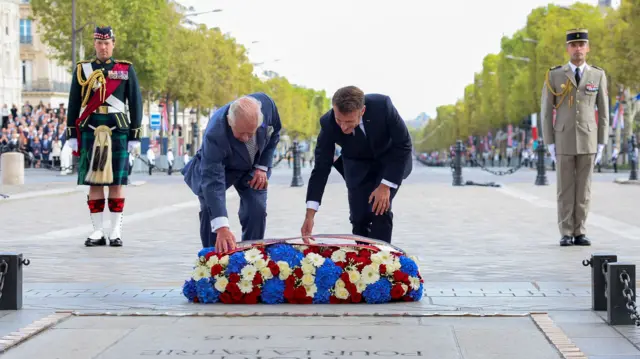 King Charles and Emmanuel Macron lean down towards wreath