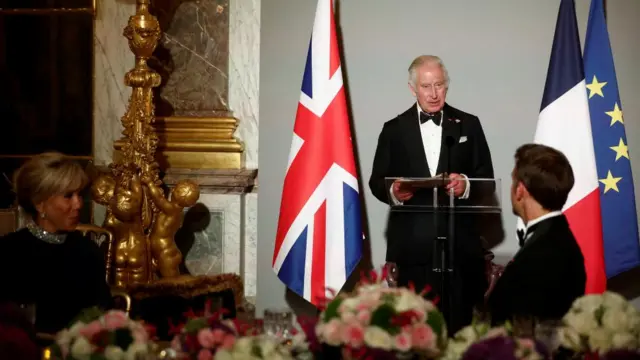 King Charles looks at Macron as he delivers a speech