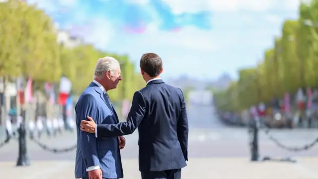 Macron puts his arm around the King as they watch the flyover