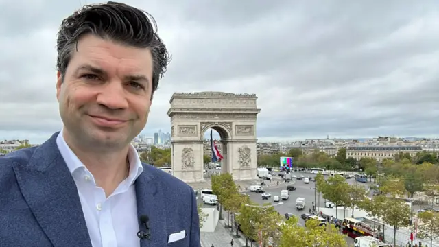 Lewis smiles from a vantage point looking down at the Arc de Triomphe