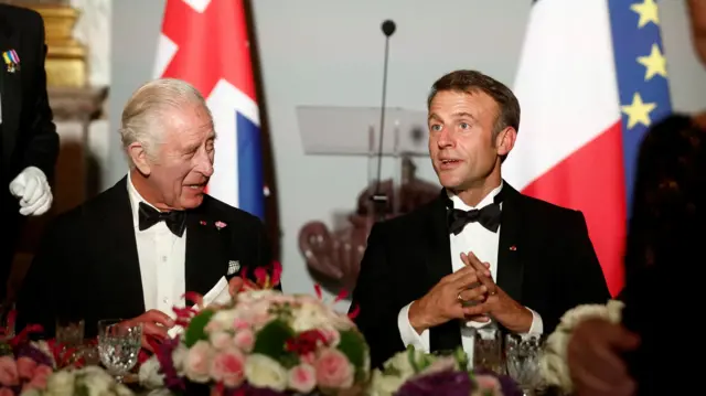 King Charles and Emmanuel Macron sit laughing next to one another