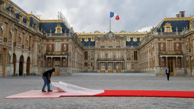 A man takes a plastic sheet off a red carpet outside the palace