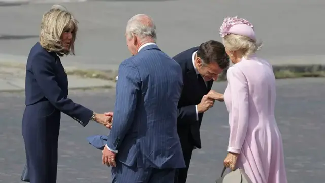 Macron kisses the hand of Camilla while Charles and Brigitte shake hands