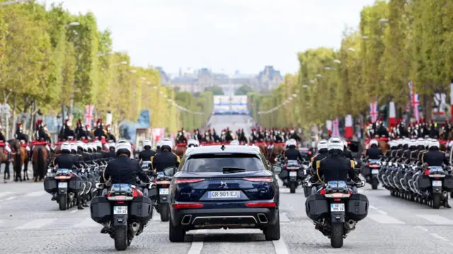 A convoy of cars, led by mounted cavalry, drives down the Champs de Elysee