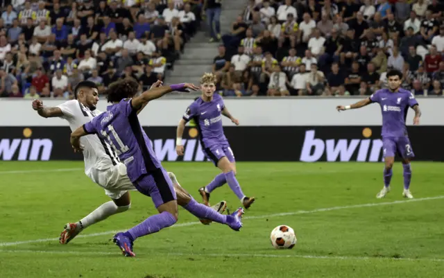 Salah slides in Liverpool's third goal under pressure from a defender.