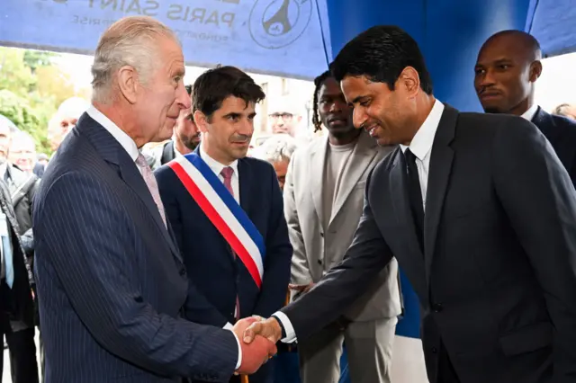 The King shakes hands with the president of Paris Saint Germain, Nasser al-Khelaifi, while Didier Drogba stands in the background