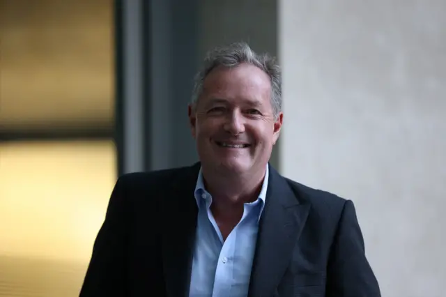 Piers Morgan with a smile on his face, wearing an open collared shirt