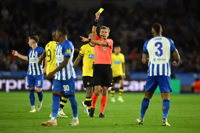 The referee brandishes another yellow card from the middle of the field.