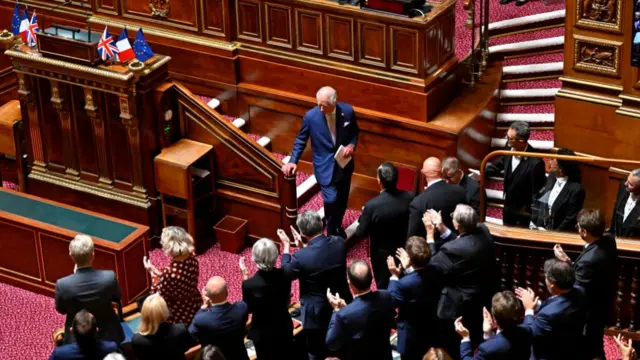 King Charles walking down the steps of the platform he gave his speech on in then French Senate chamber. The assembled politicians are giving him a standing ovation.