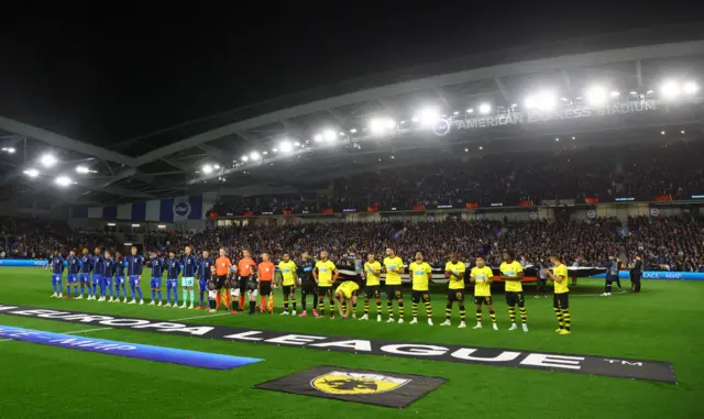 Brighton and Athens players line up for the anthem before kick off.