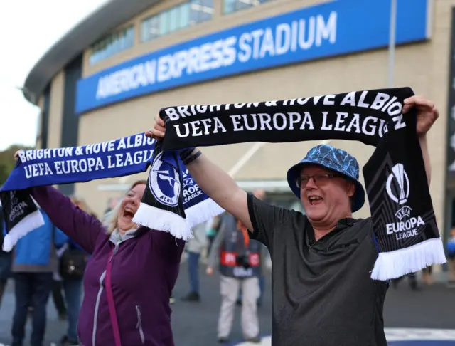 Brighton fans hold half club colour and Europa League scarves aloft outside the AMEX.