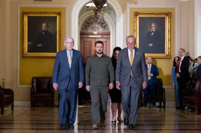 President Zelensky walking through a room with Mitch McConnell and Chuck Schumer