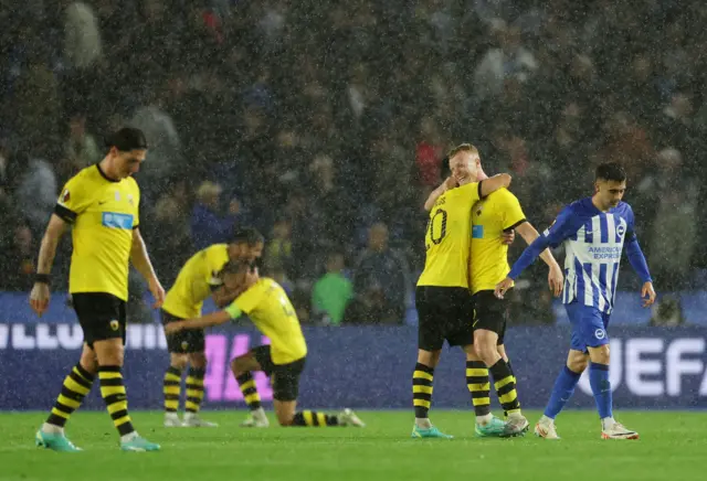 Aek players embrace one another after their victory as Brighton players trudge away.