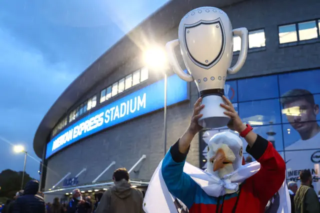 A Brighton fan with a seagull mask holds aloft a blow up trophy.