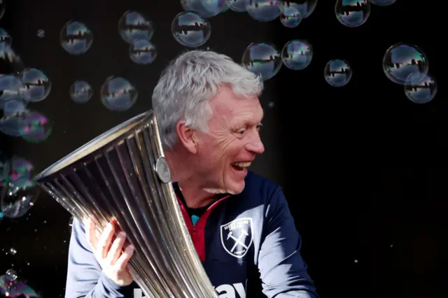 David Moyes smiles and poses with the Europa Conference League trophy.