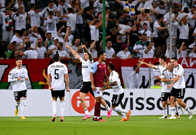 Warsaw players swarm a Villa defender as they run to celebrate.