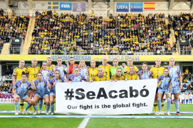 Spain and Sweden players stand behind a banner of support for the Se Acabo movement.