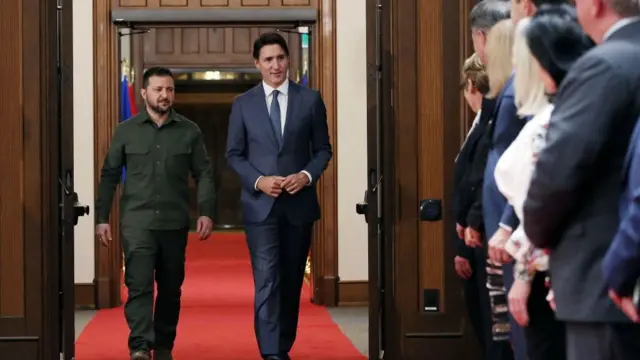 Trudeau and Zelensky walks down a hallway where a group of people stand in line