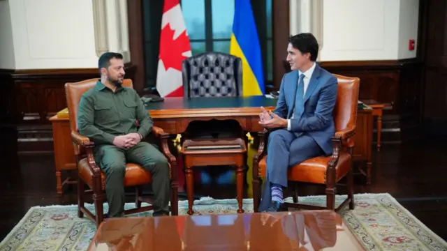 Both men are sat in leather chairs, mid-discussion