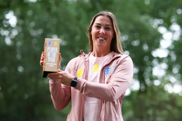 Mary Earps holds aloft her Player of the Year trophy while looking into the camera.