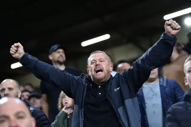 A fan cheers with his arms above his head.