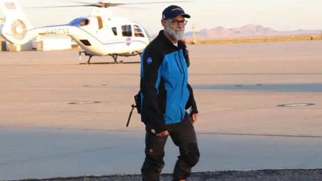 Dante Lauretta, the chief scientist on the project walking in front of a helicopter