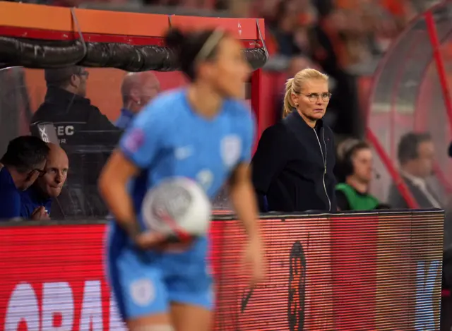 Wiegman watches on from behind an advertising board on the sideline.