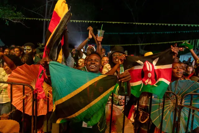 Ugandan Nyege Nyege festival-goers wave flags of Tanzania and Kenya at the Itanda Falls on the second day of Nyege Nyege festival, the annual four-day international music festival, in Jinja, on September 16, 2022. - Uganda said on September 12, 2022, that it would allow a popular music festival to go ahead this month, reversing a ban imposed over claims the event promoted sex, homosexuality and drug use.