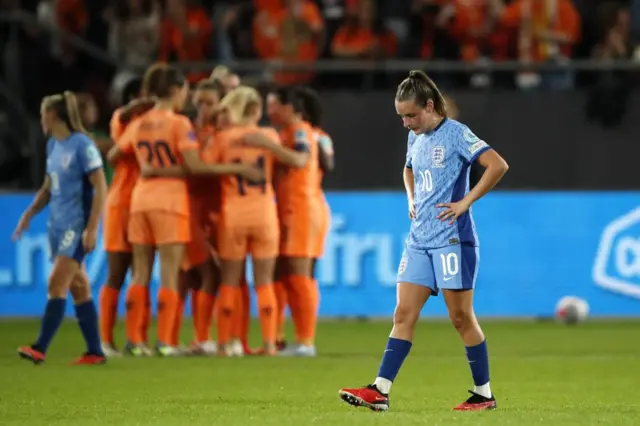 Toone stares down to the floor with her hands on her hips as the Dutch celebrate in the background.